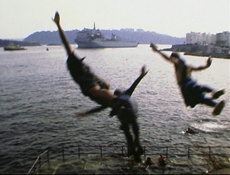 still from the Super 8mm film Sea Front, showing 3 tombstoners leaping off Plymouth Hoe, with warship and view across to south east Cornwall beyond